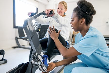 African american occupational therapist explaining a patient how to use the static bicycle and patient listening very careful